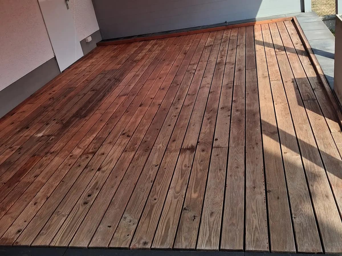 Überdachte Holzterrasse mit gereinigten, gleichmässig nachgedunkelten Dielen und rotem Sonnensegel.