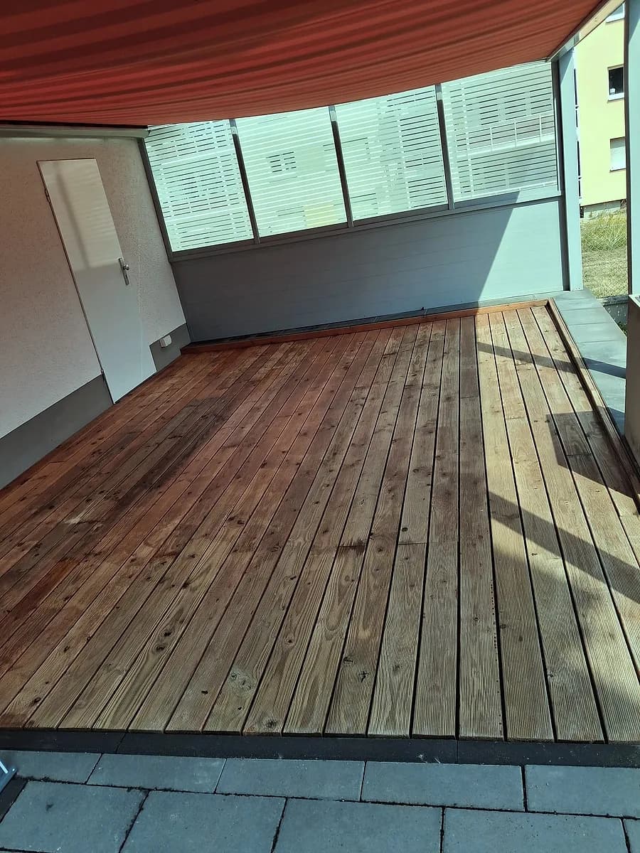 Überdachte Holzterrasse mit gereinigten, gleichmässig nachgedunkelten Dielen und rotem Sonnensegel.