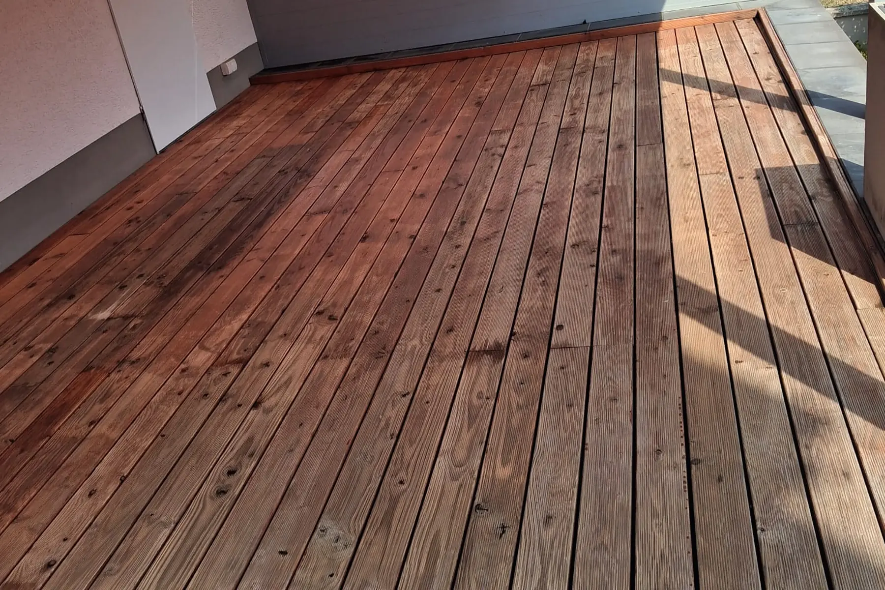 Gereinigte Holzterrasse mit gleichmässig nachgedunkelten Dielen unter einem Sonnensegel.